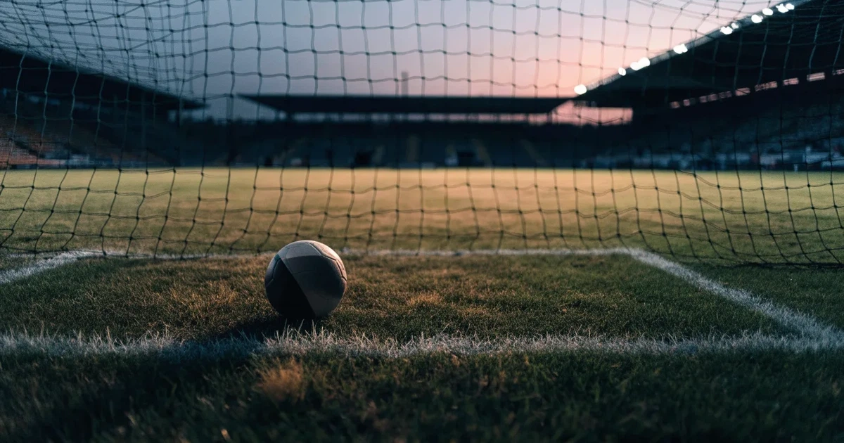Ein Fußball liegt im Strafraum direkt vor dem Tor mit Netz, im Hintergrund leere Ränge bei Dämmerung.